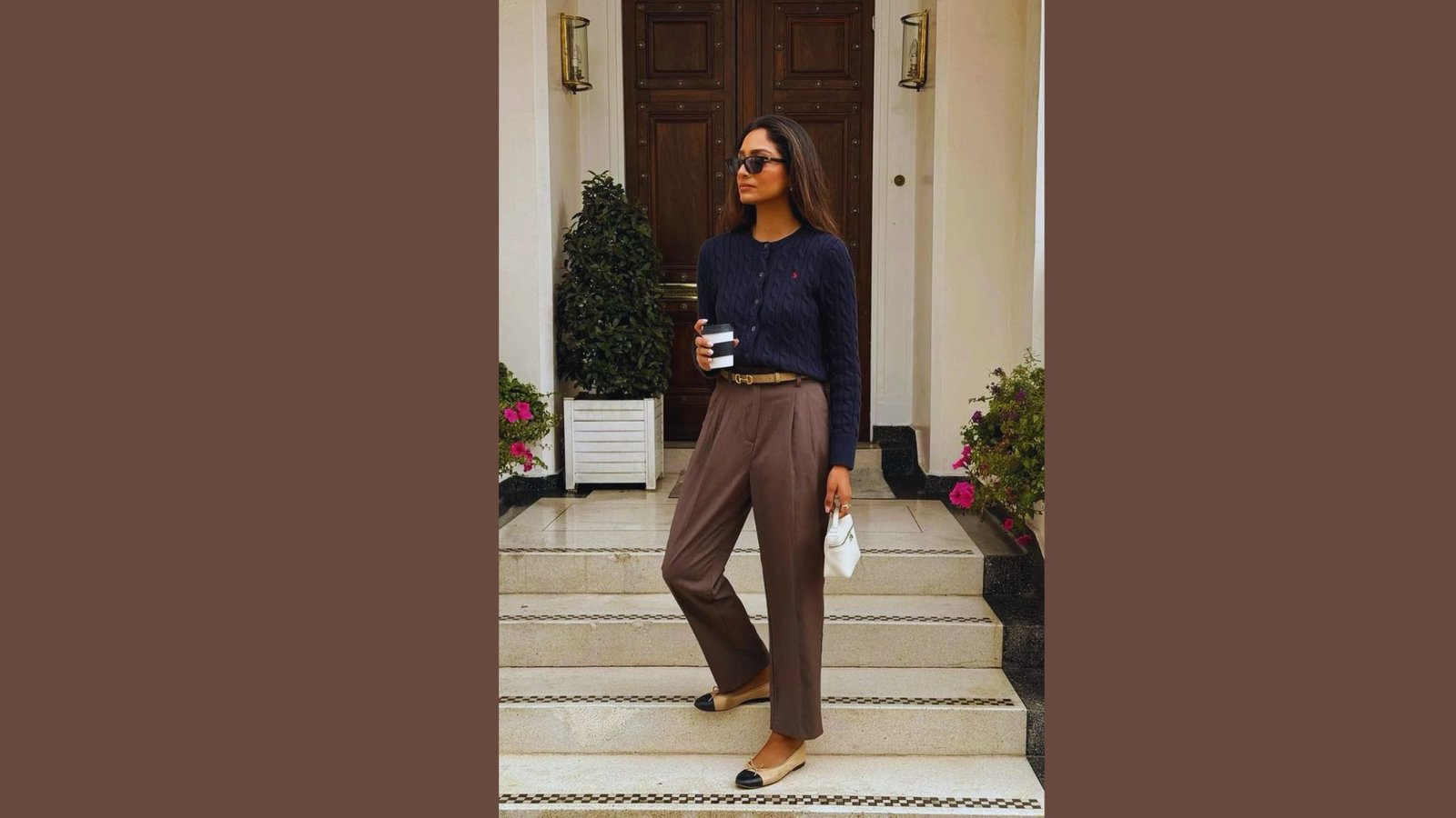 A woman wearing a black top and brown pants stands confidently, showcasing a casual yet stylish outfit.