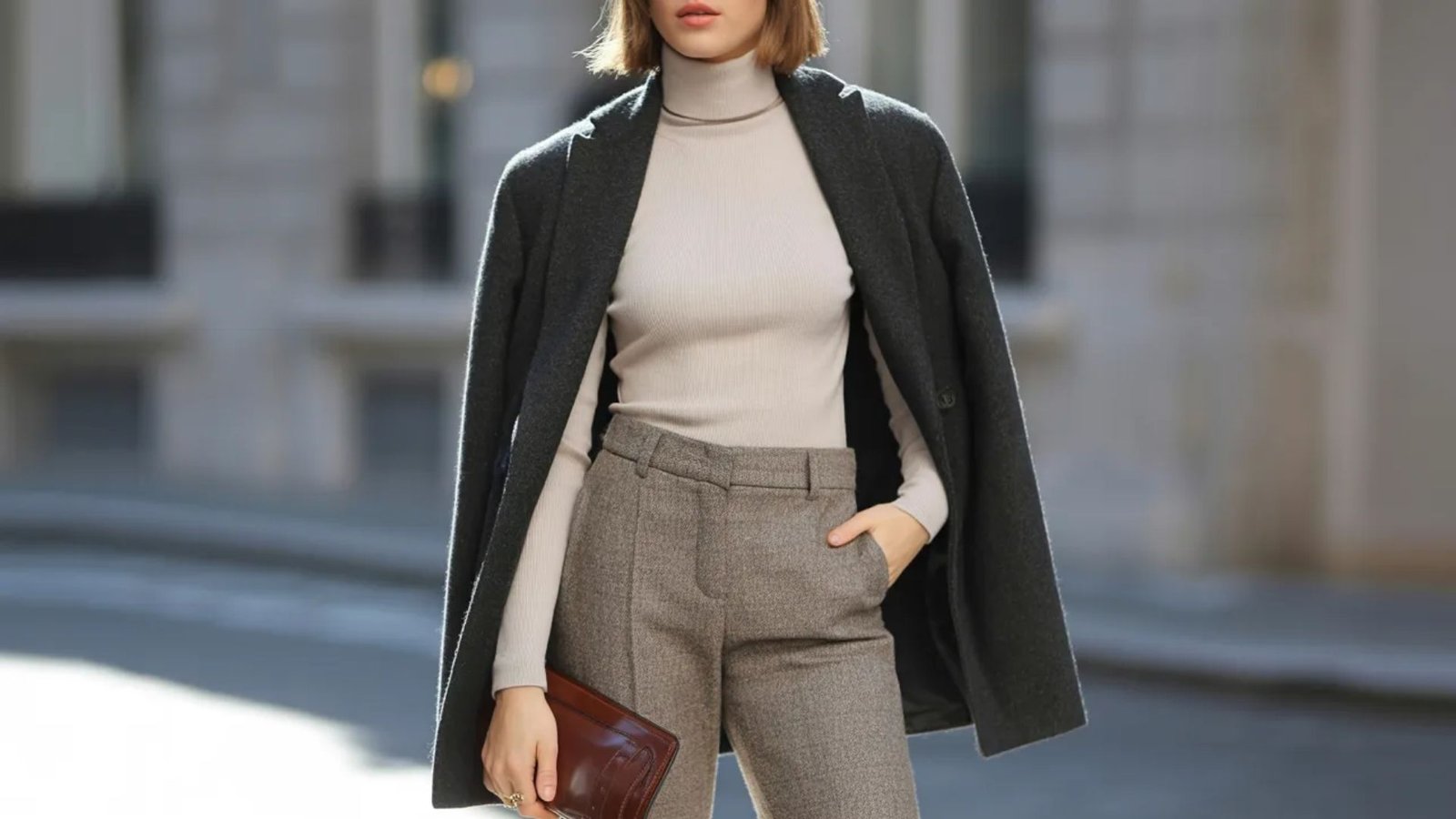 A woman wearing a turtleneck sweater and pants, standing confidently with a neutral background.
