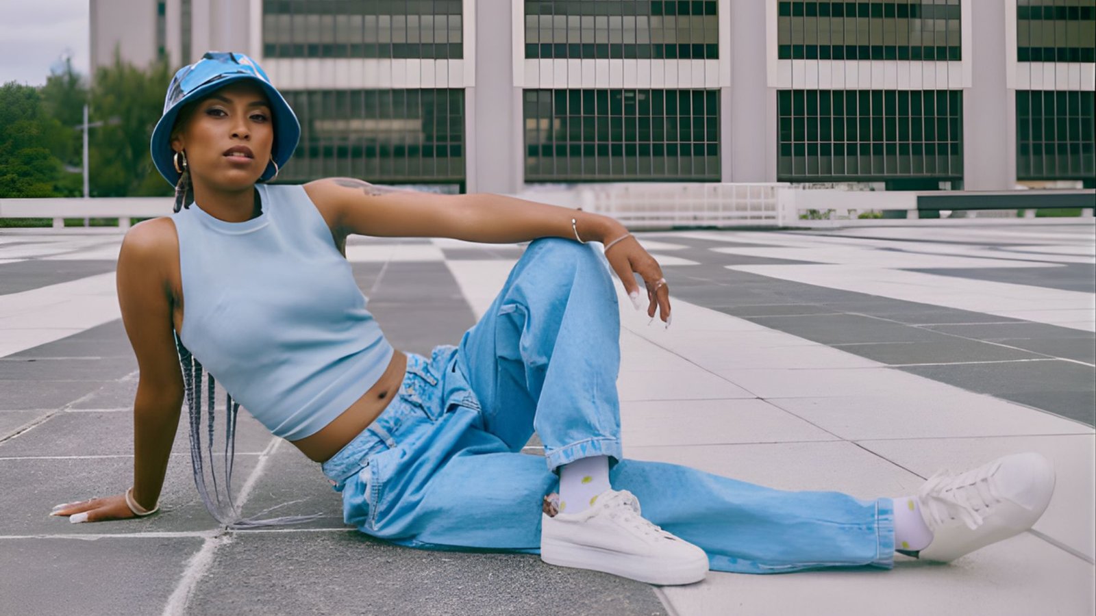 A woman in blue jeans and a hat is seated on the ground, appearing calm and at ease in her surroundings.