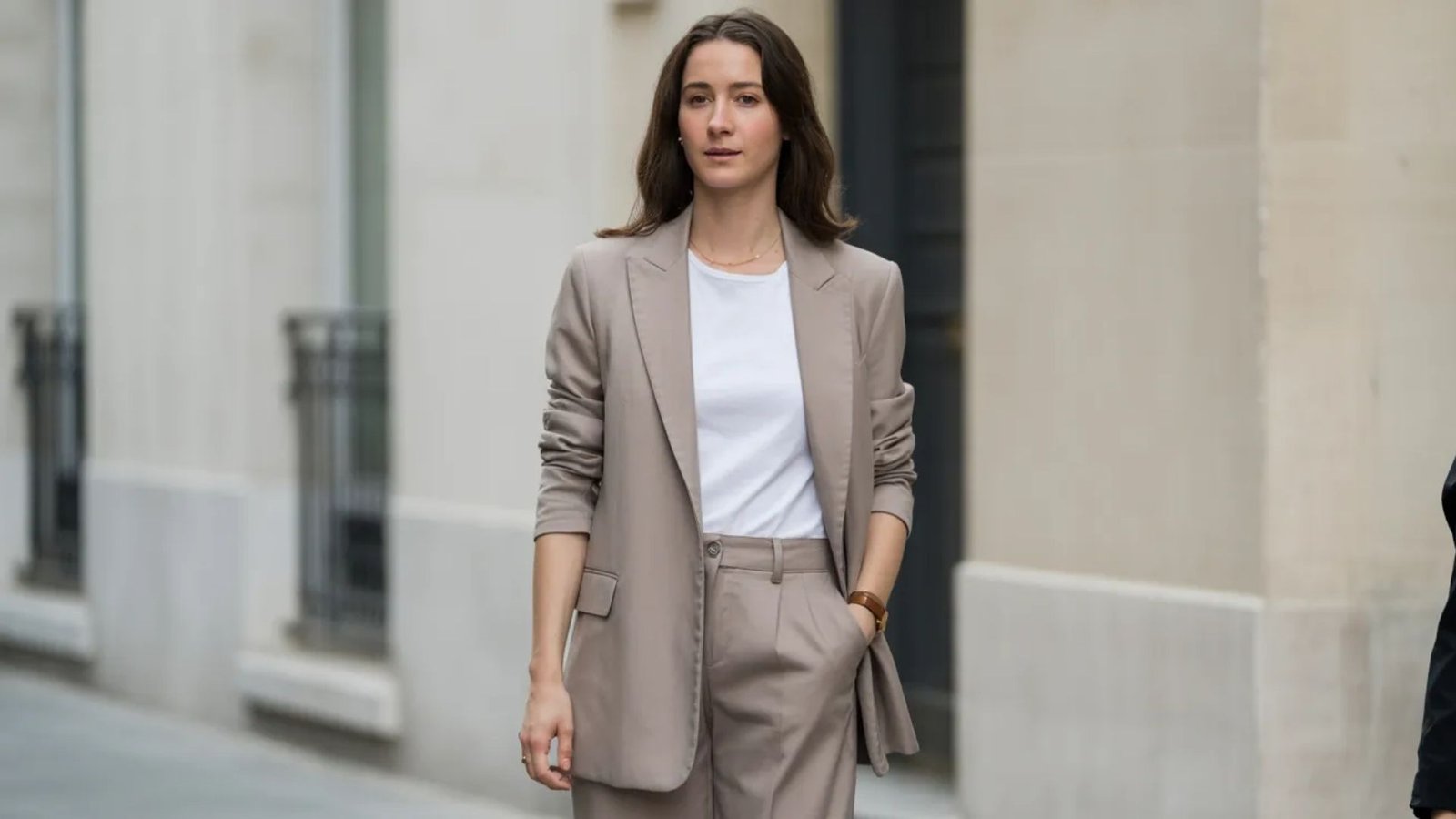 A woman in a suit and white shirt confidently walks down the street, showcasing a professional appearance.