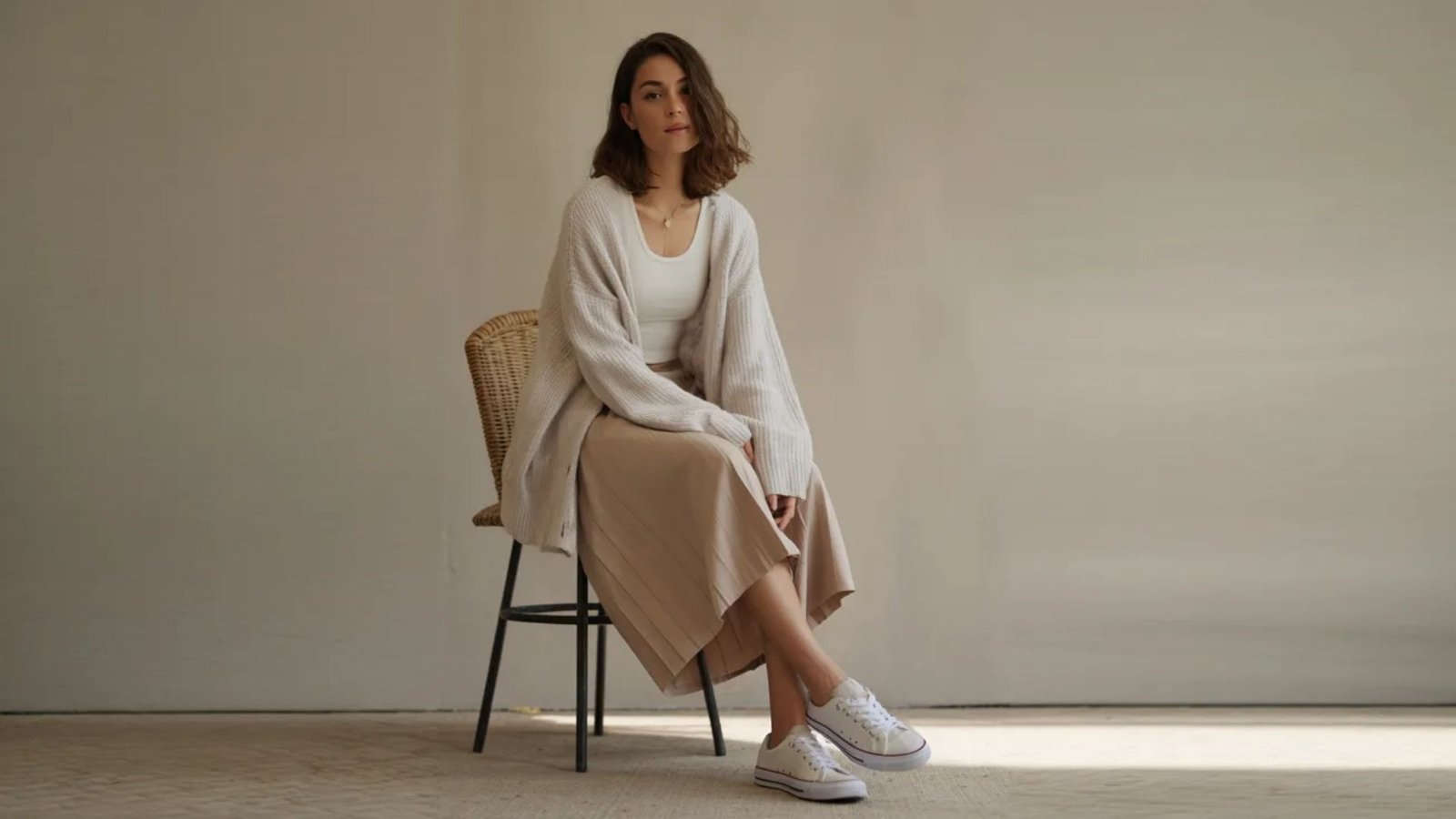 A woman in a white shirt and long skirt sits on a chair, looking relaxed and composed.