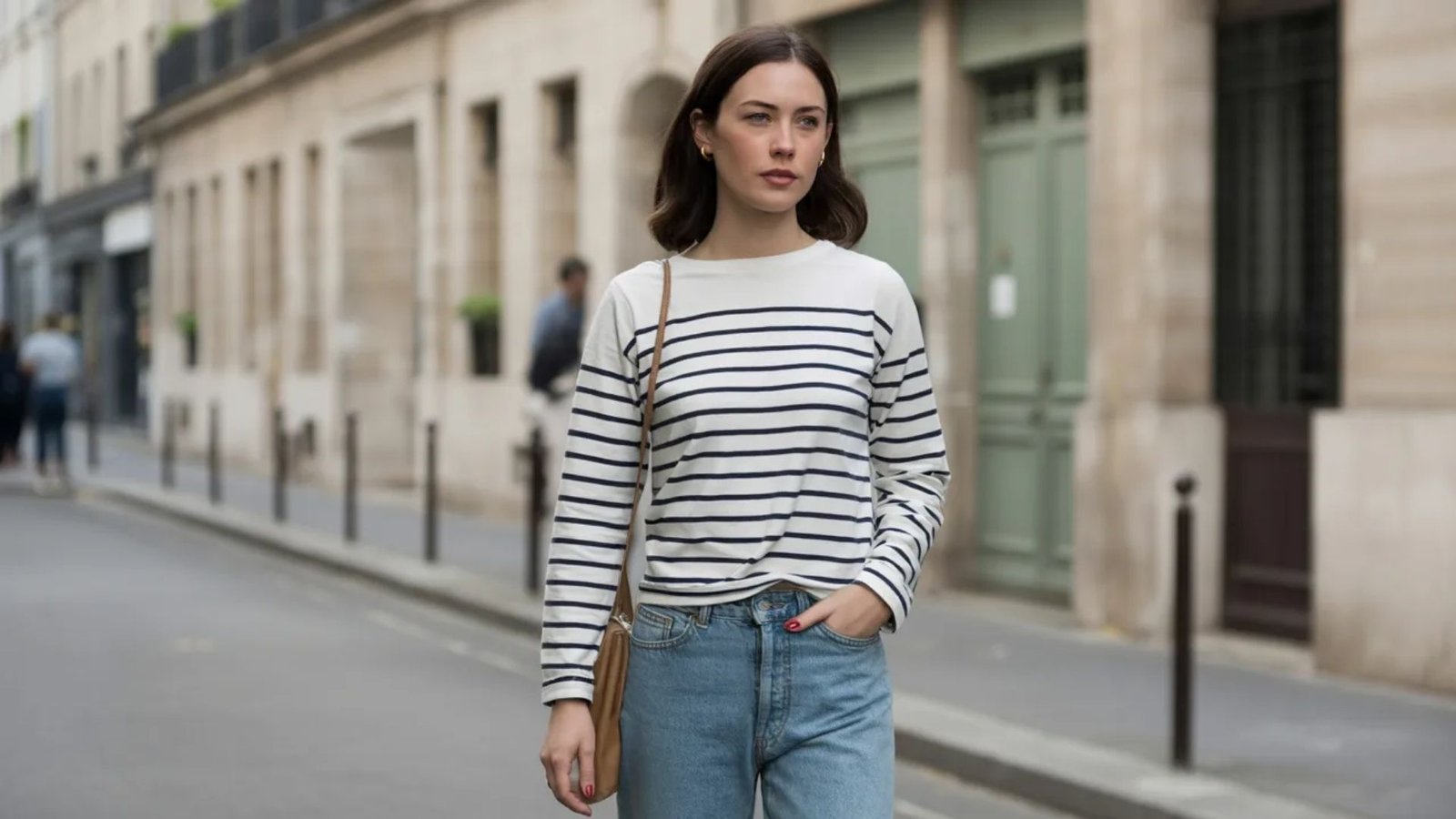 A woman in a striped shirt and jeans walks down a city street, surrounded by buildings and greenery.