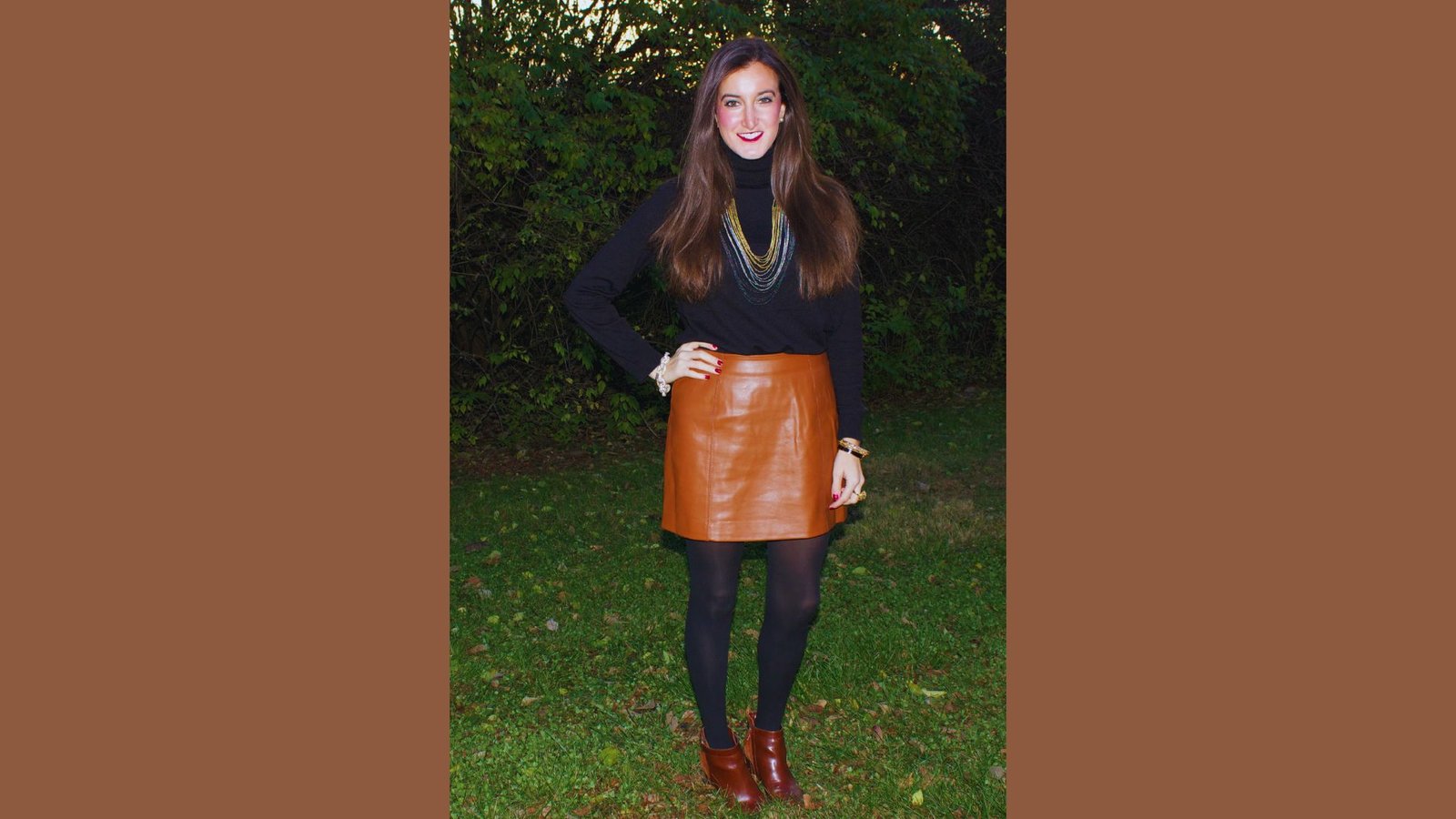 A woman wearing a black sweater and a brown leather skirt stands confidently, showcasing her stylish outfit.