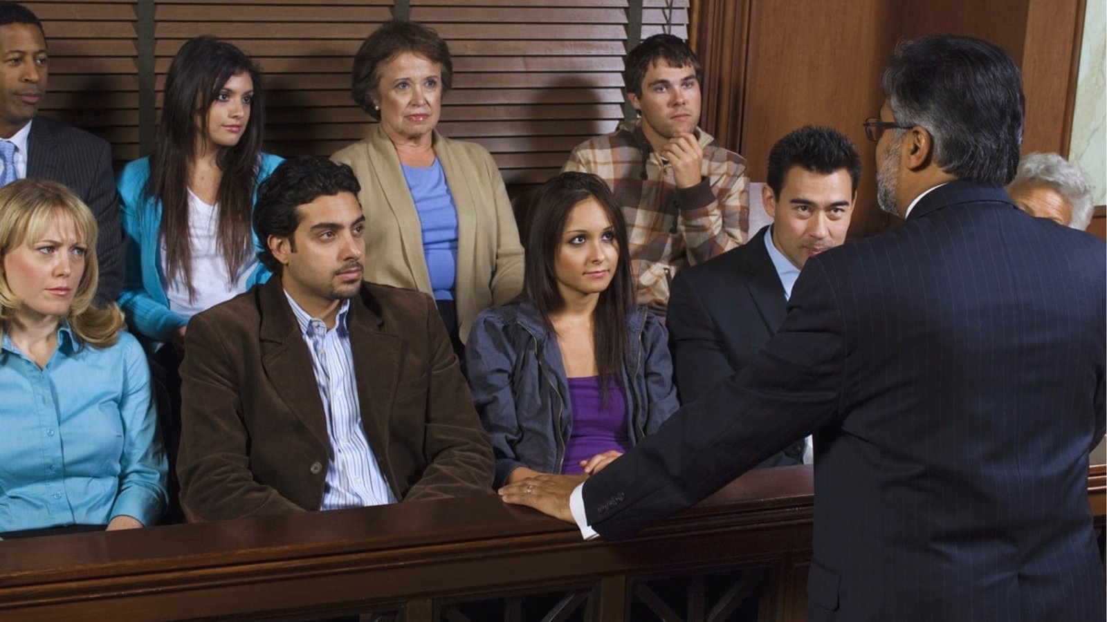 A diverse jury attentively listens to a lawyer in a courtroom. The setting is serious, and the expressions range from focused to slightly concerned.