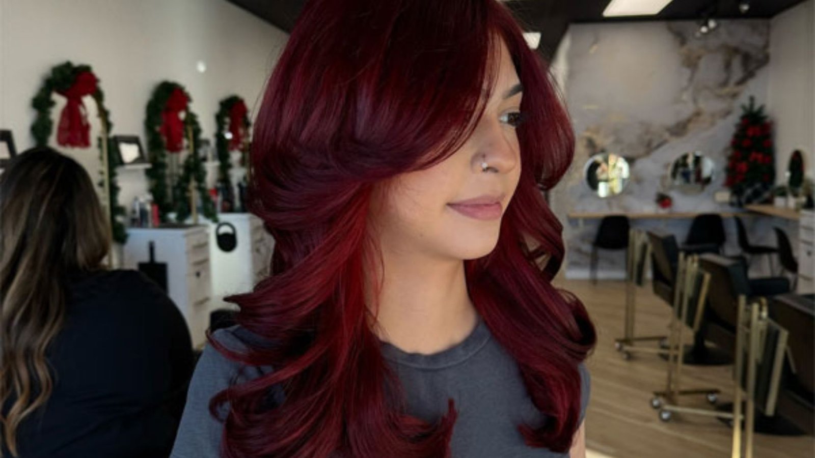 A woman with red hair styled in a Cherry Butterfly Cut at a salon, showcasing her vibrant hair and professional setting.
