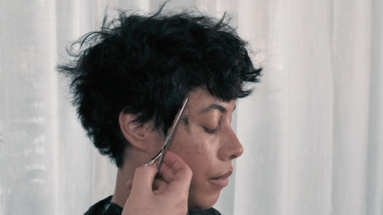 A woman receiving a haircut, with scissors in use, emphasizing the importance of regular hair trimming.