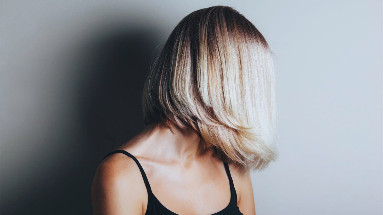 Side profile of a sleek layered French bob without bangs in blonde balayage with dark roots, chin-length with flipped-under ends