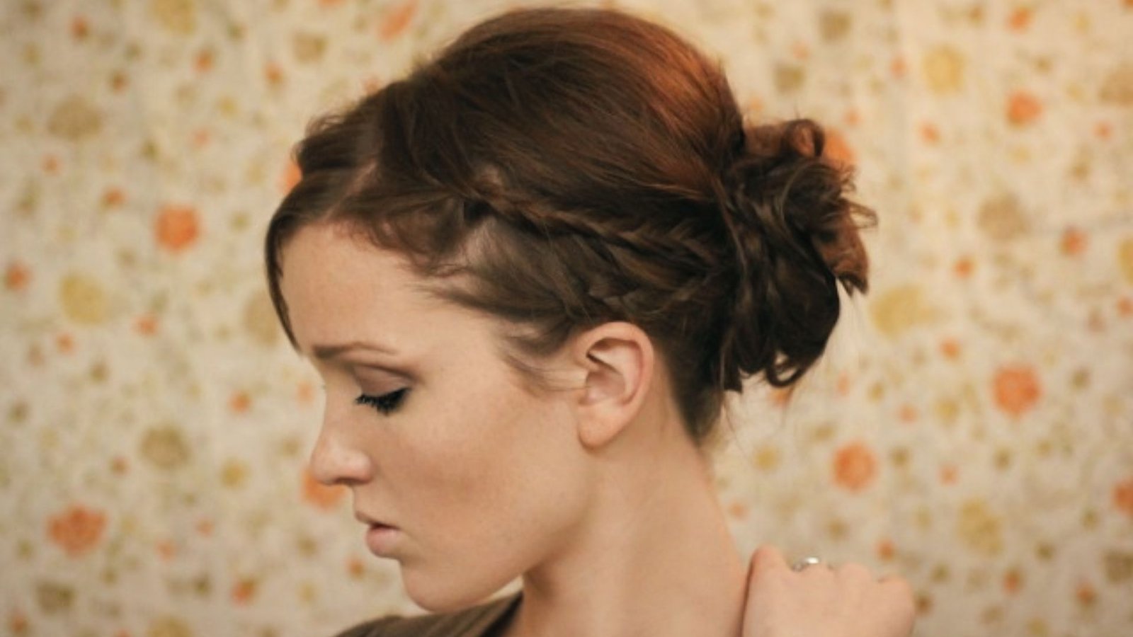 A woman with a braided messy bun and side bangs, showcasing a stylish and casual hairstyle.