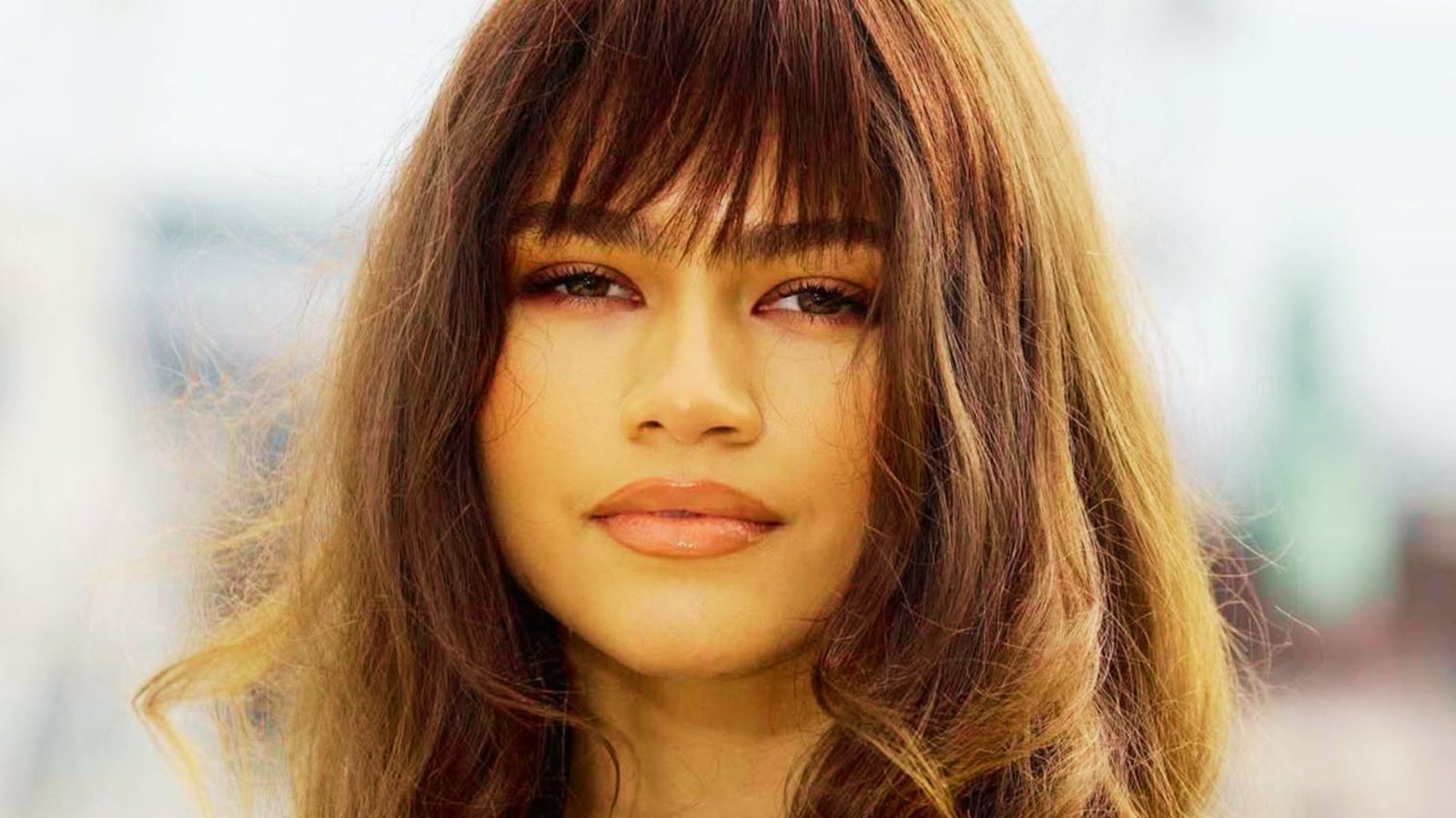 A woman with long hair styled with Bardot bangs, complementing her round face shape.
