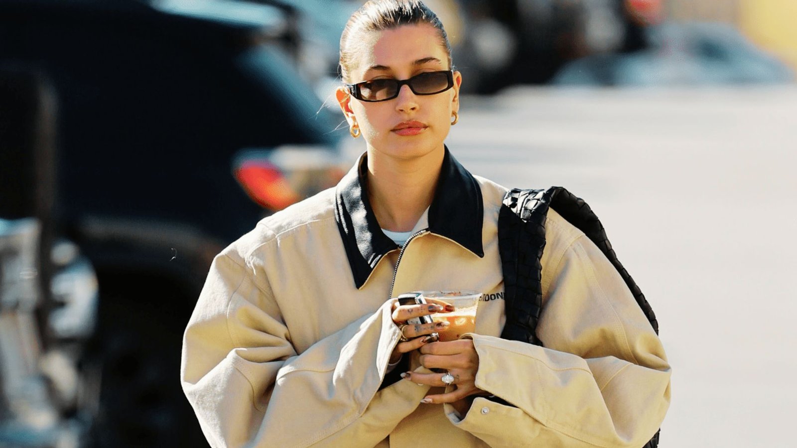 A stylish woman in sunglasses and a trench coat enjoys coffee, showcasing a blend of comfort and contemporary soccer mom fashion.