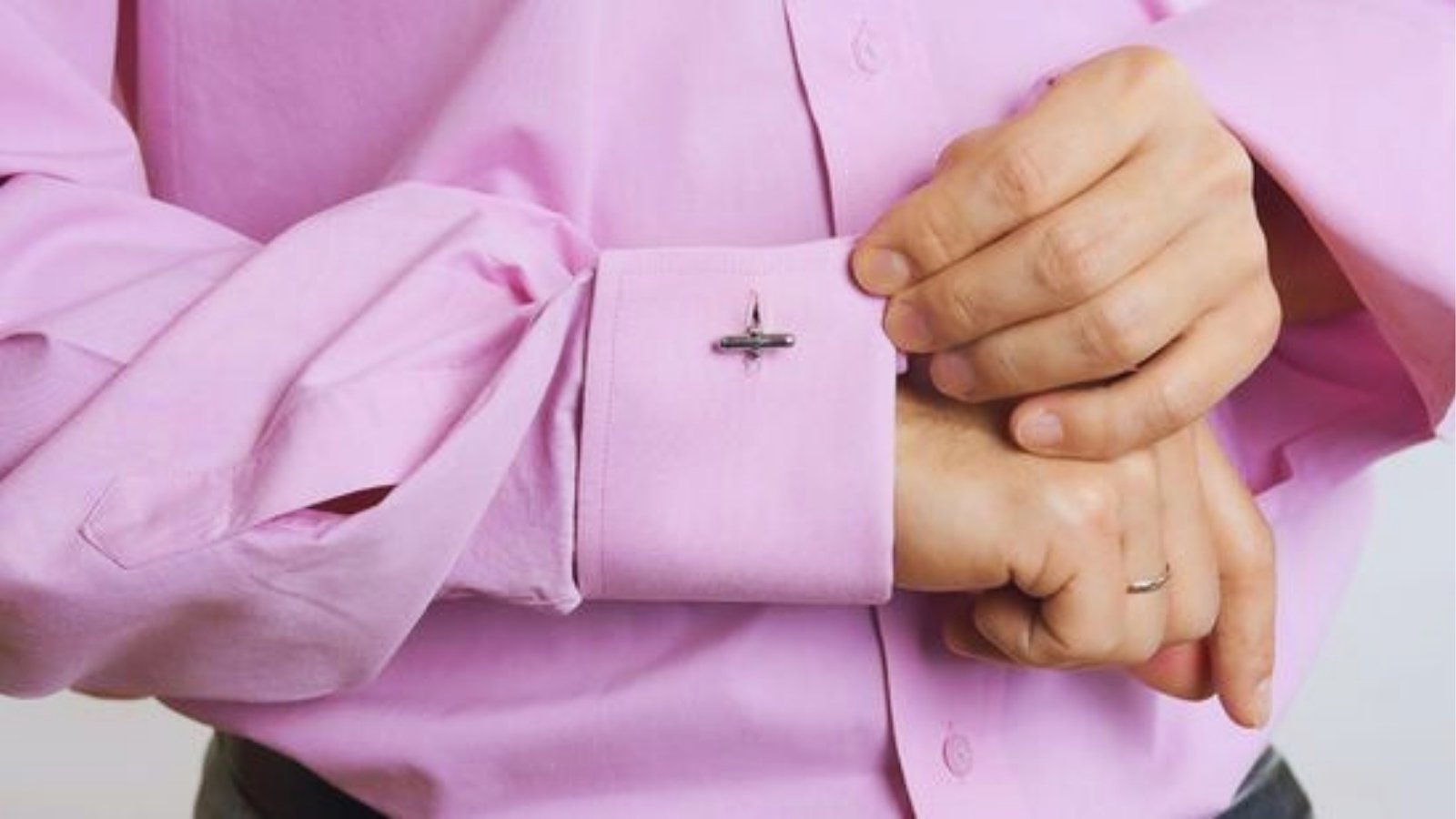 Person fastening cufflink on pink French cuff shirt demonstrating how to wear cufflinks
