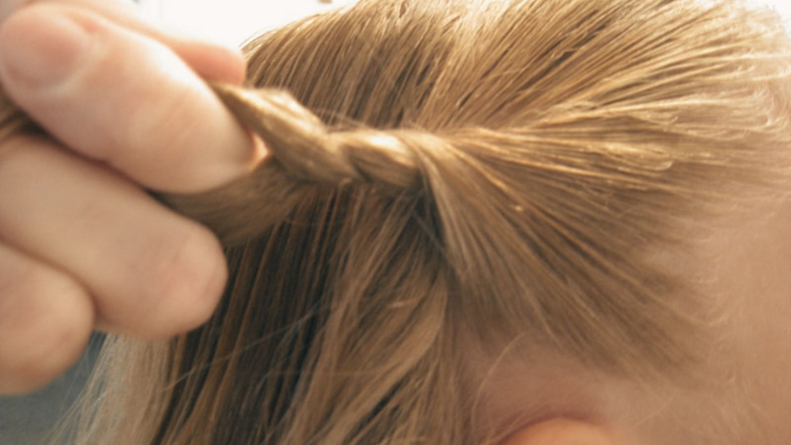 A person braids a child's hair, incorporating twisted front sections and bangs for a stylish look.