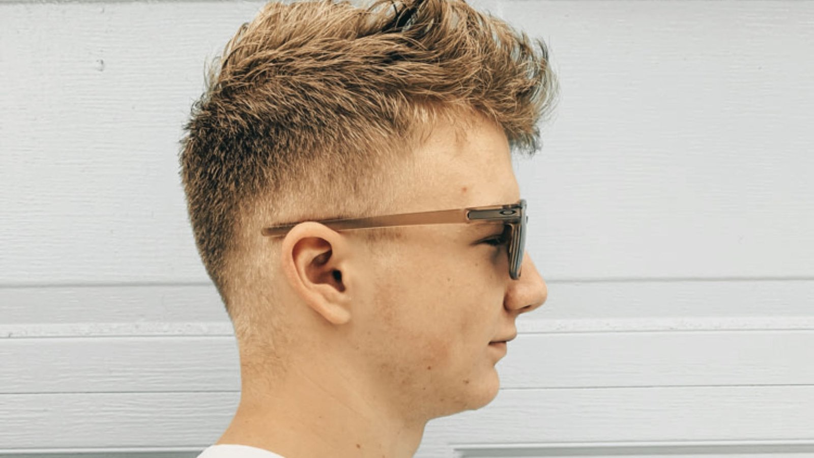 A young man with a faux hawk disconnected undercut fade hairstyle, wearing sunglasses.
