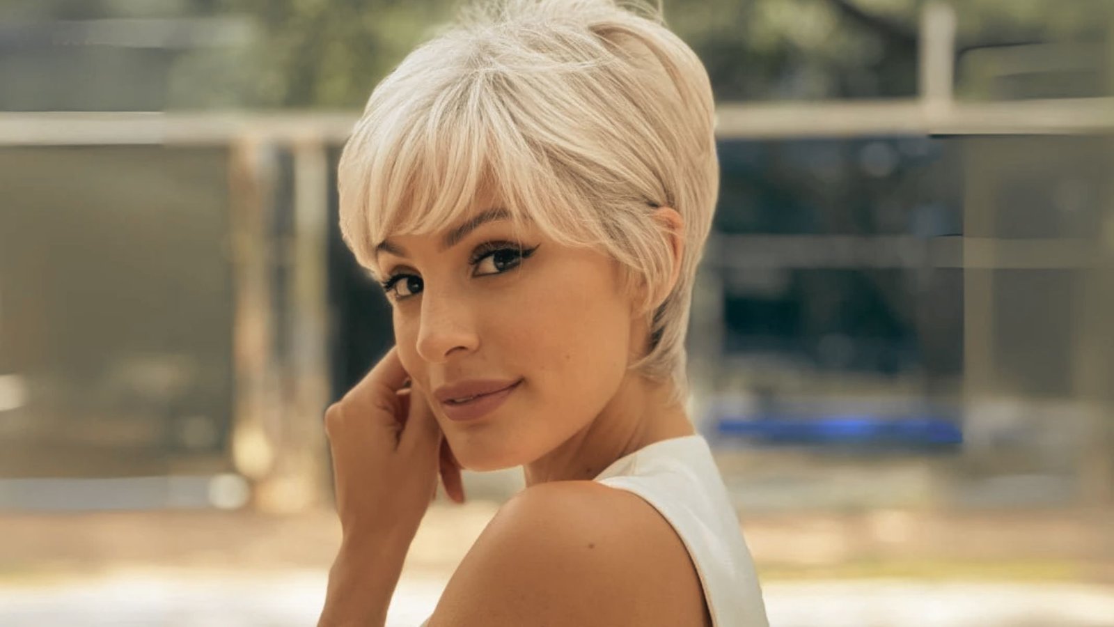 A woman with short blonde hair styled in a textured pixie cut, wearing a white top.