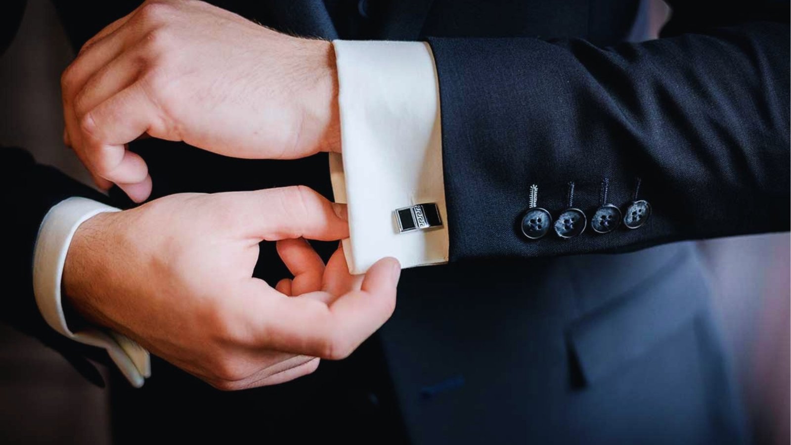  Man fastening cufflinks on white French cuff shirt while wearing dark suit for formal styling guide
