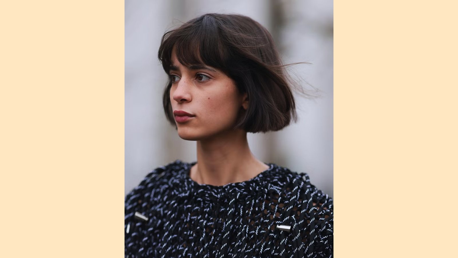Windswept dark brown French bob with wispy eyebrow-skimming bangs and textured jaw-length cut
