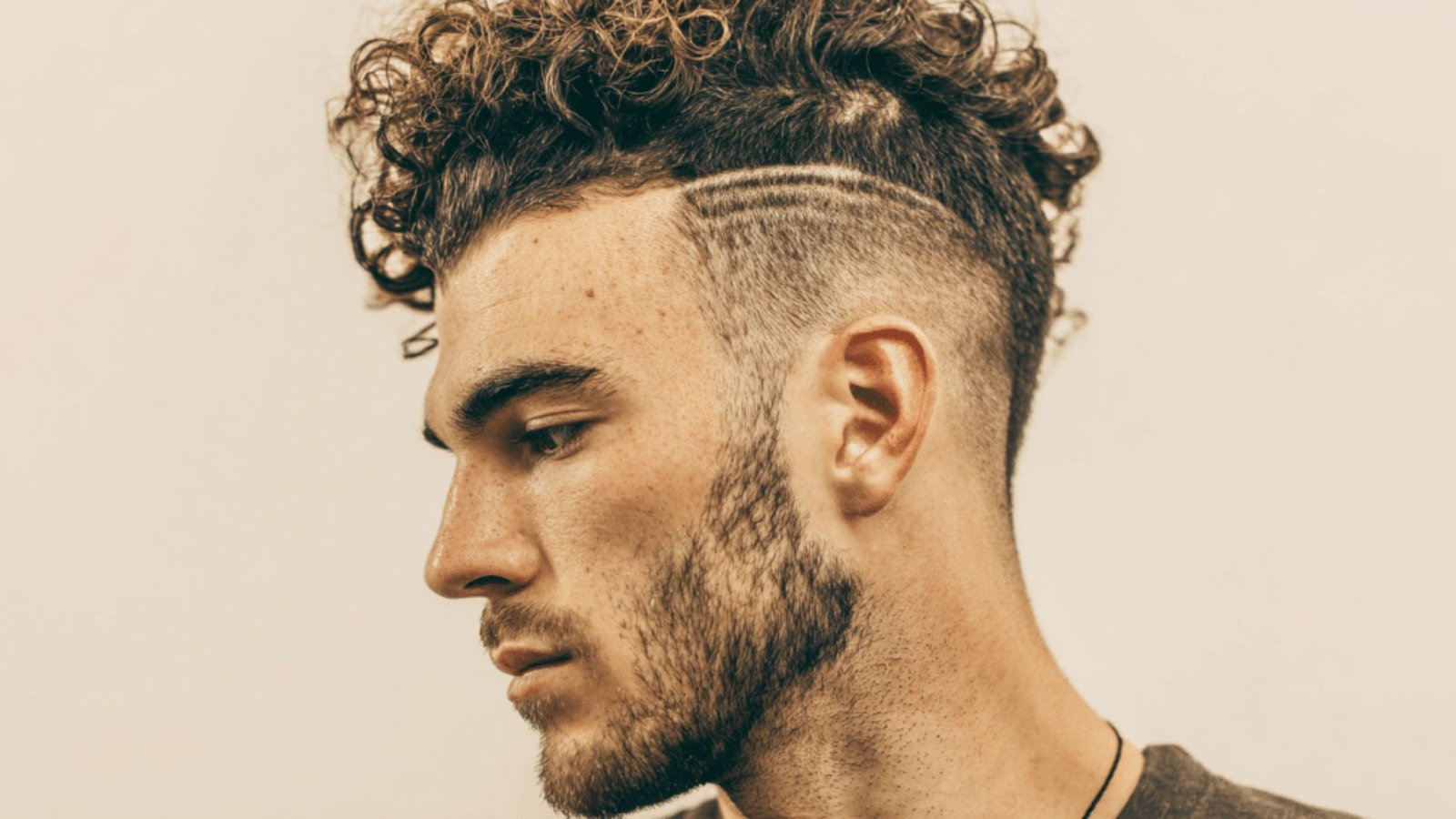 A man with a curly haircut and beard, featuring a perm disconnected undercut fade style.