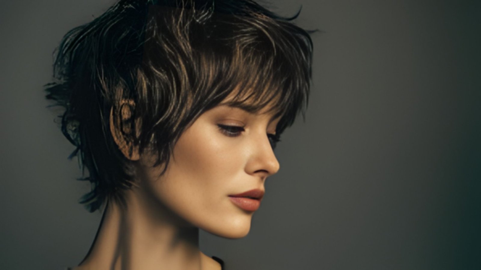 A woman with short, shaggy hair and bangs stands against a dark background, showcasing a retro hairstyle