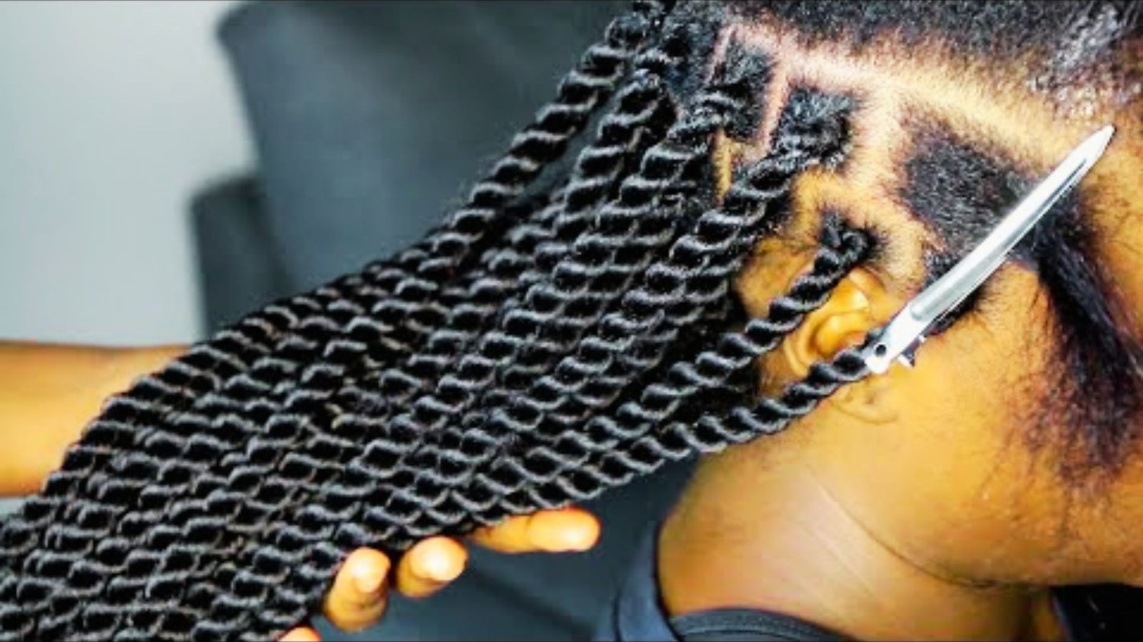 A woman has her hair braided while holding a pair of scissors, illustrating tools needed for hair styling.