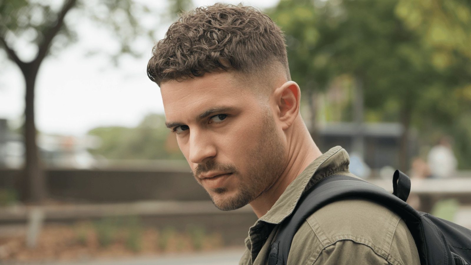 A man wearing a green shirt and a backpack, sporting a crew cut disconnected undercut fade hairstyle.