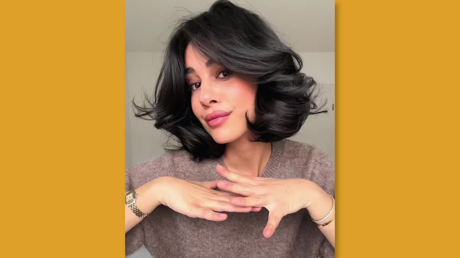 Voluminous black shoulder length bob haircut with flipped ends and side part worn by woman in taupe sweater