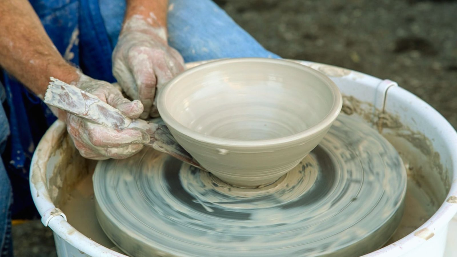 Hands shape a clay bowl on a spinning pottery wheel, creating smooth, even curves. The scene conveys focus and creativity with earthy tones.