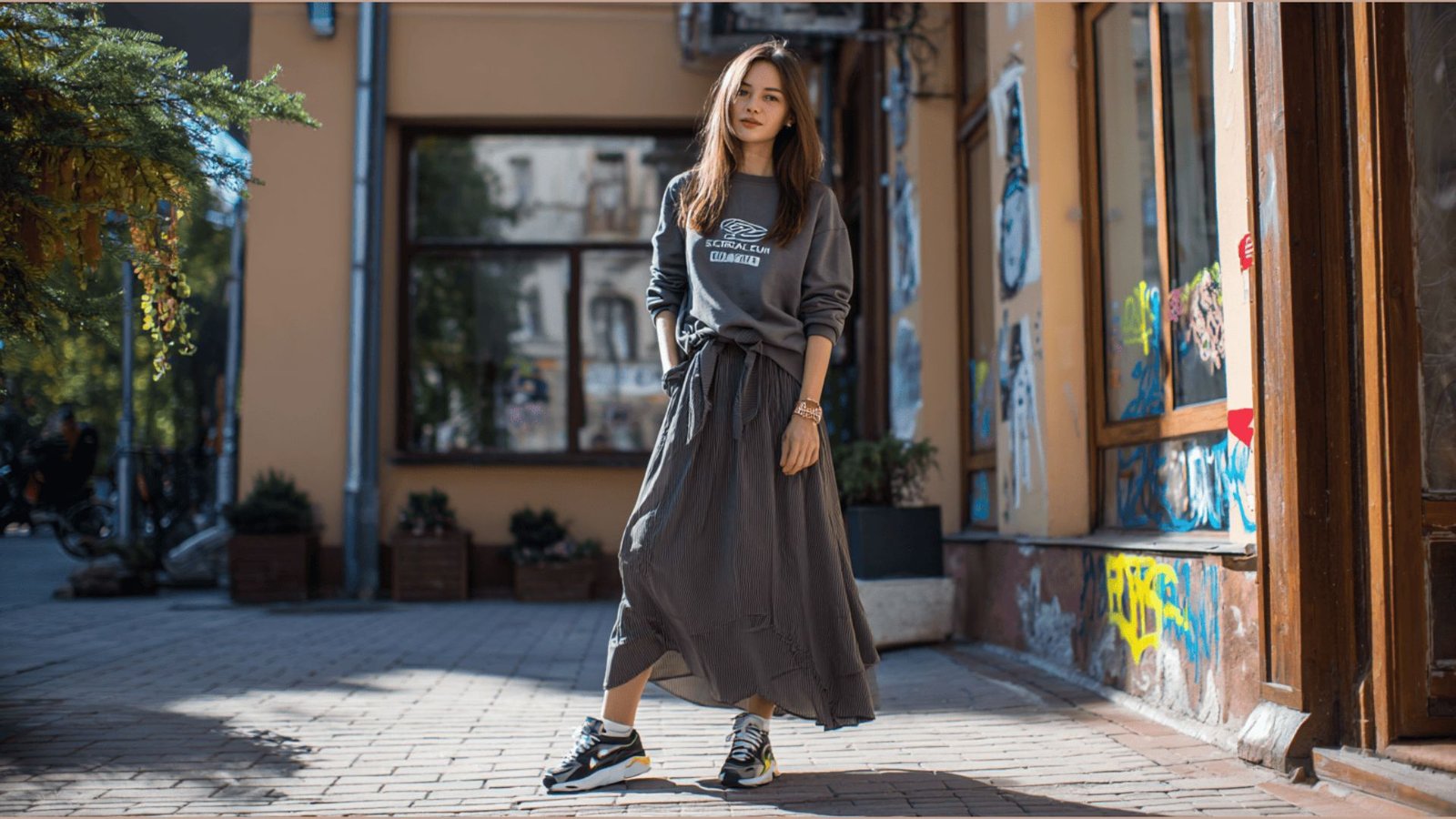 Woman styled in a grey sweatshirt tied over a flowy maxi skirt with sneakers. Casual everyday comfort outfit for stay at home moms running errands or at home. 

