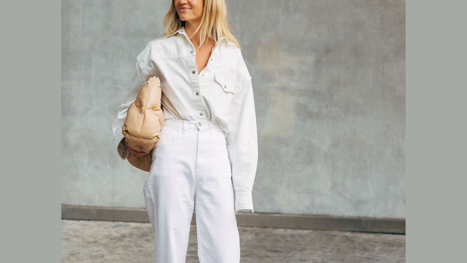 All-white 90s mom outfit with oversized button-up shirt tucked into high-waist jeans. Styled with a tan clutch for a clean, minimal look.