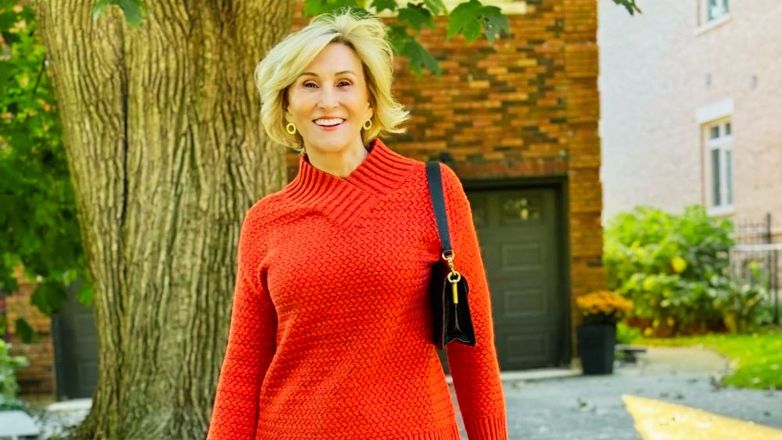 A woman wearing an orange sweater and black skirt, paired with leggings and slip-on shoes, stands confidently.