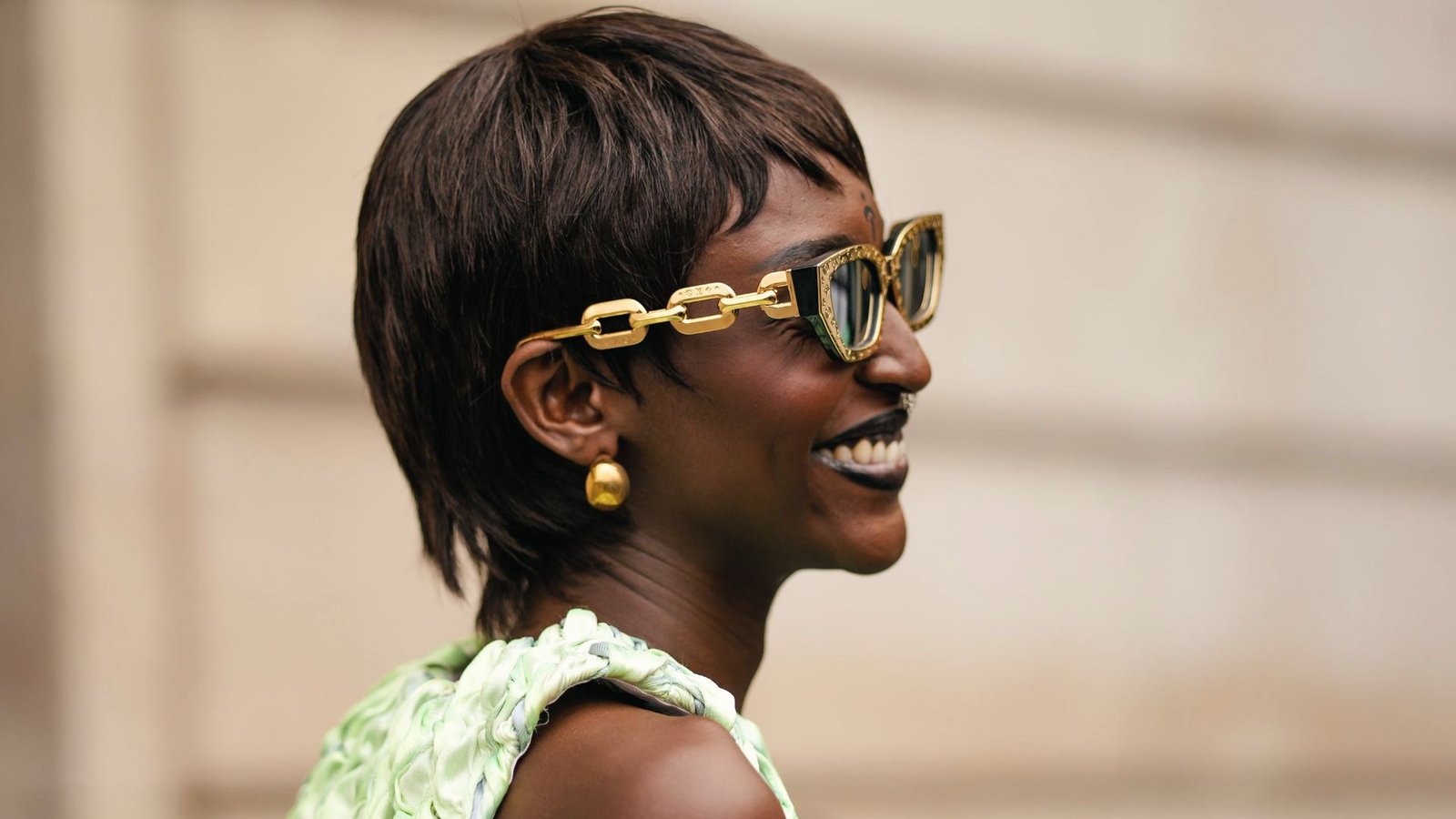 A woman in sunglasses and a green dress, showcasing a stylish shaggy choppy pixie cut.