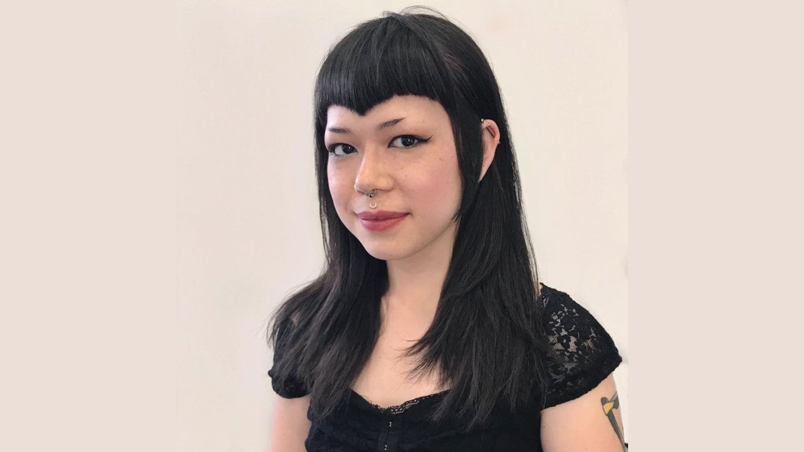 Woman with long black hair and blunt bangs featuring a widow’s peak detail.
The fringe is cut straight across with a small pointed dip at the center hairline.