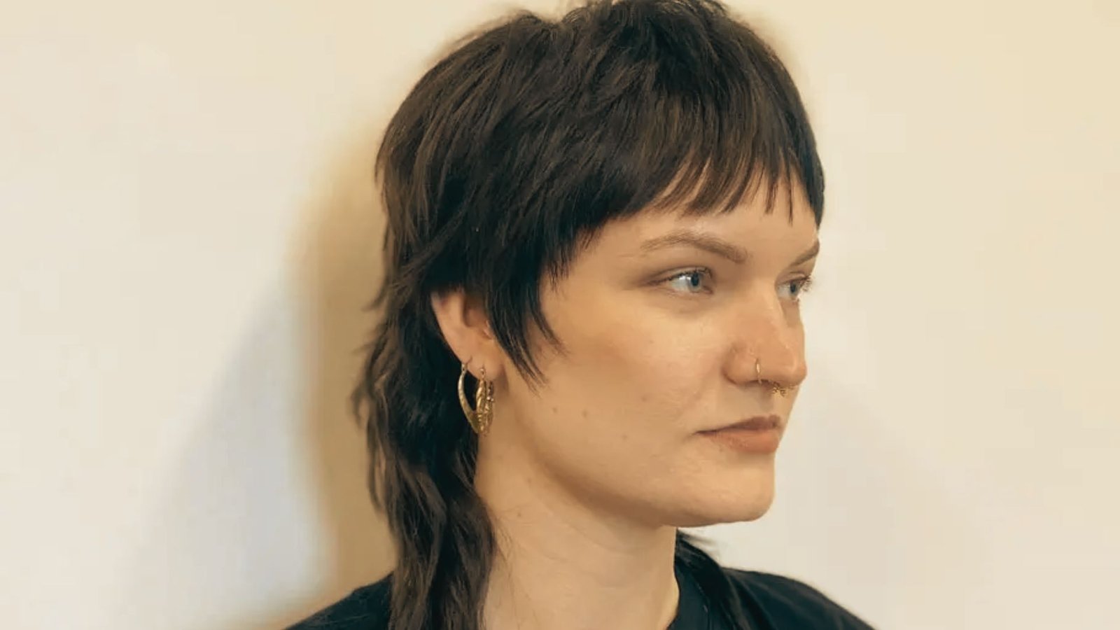 A woman wearing a black shirt and earrings, showcasing a feminine layered mullet hairstyle.