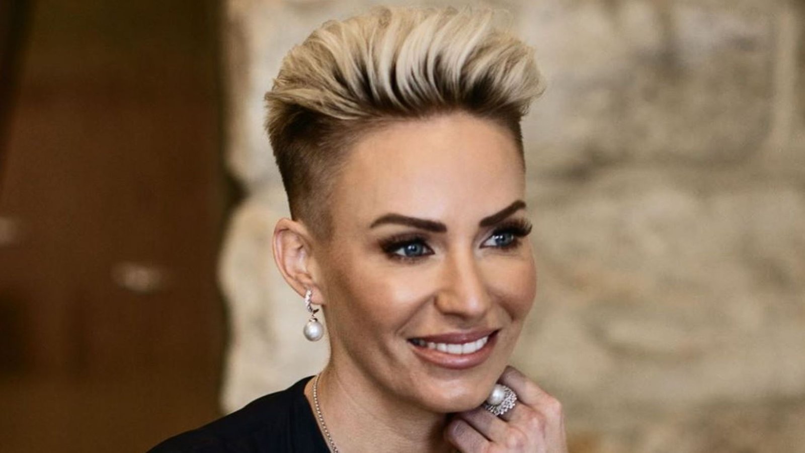 Woman with a blonde faux hawk undercut styled with height and volume on top. Sides are faded short to emphasize the sculpted, swept-up texture for a glam punk vibe.