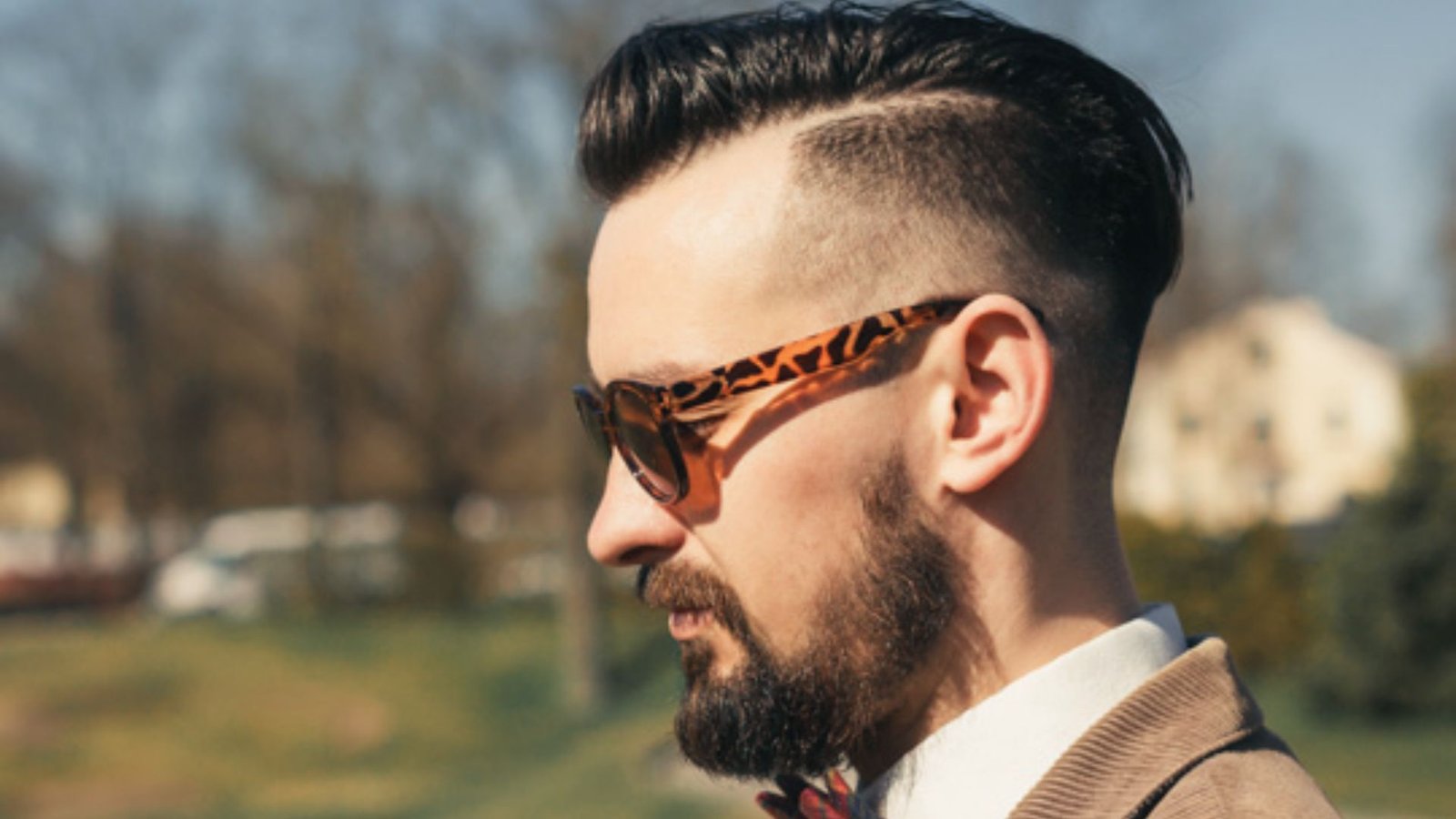 A man with a beard and sunglasses, sporting a low fade disconnected undercut hairstyle.