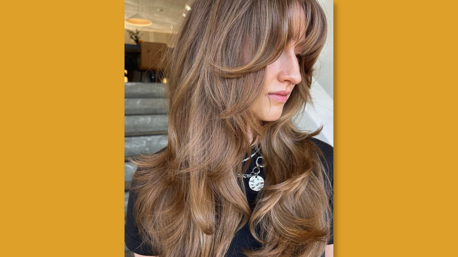 Side view of low maintenance layered medium length haircut with feathered face-framing layers and soft highlights on brunette hair for round face
