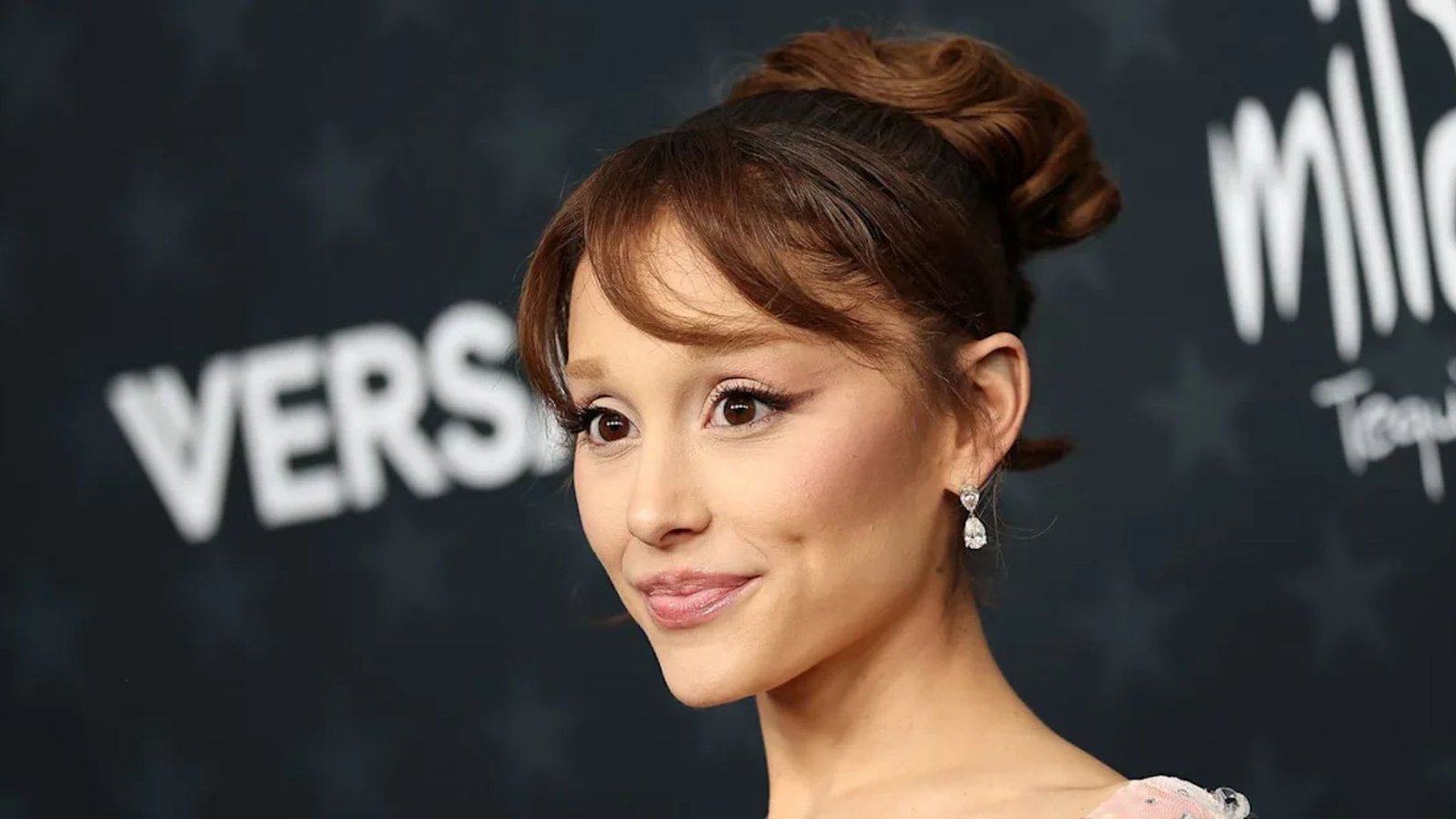Woman at a red carpet event with hair in an updo and side-swept bangs. The wispy fringe is angled across the forehead with loose face-framing pieces.