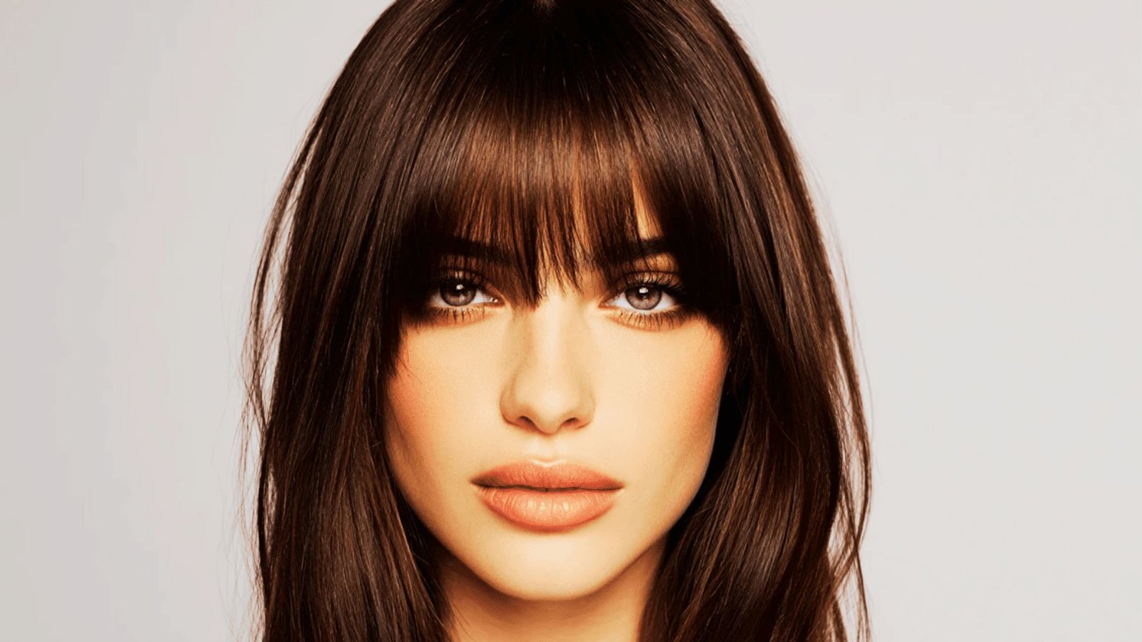 A woman with long brown hair and bangs, showcasing a hairstyle that complements her face shape.
