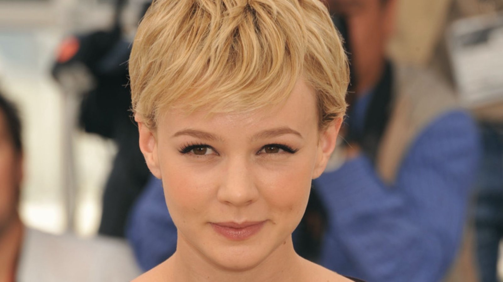 A woman with a side-swept shaggy pixie cut stands confidently, showcasing her stylish look.