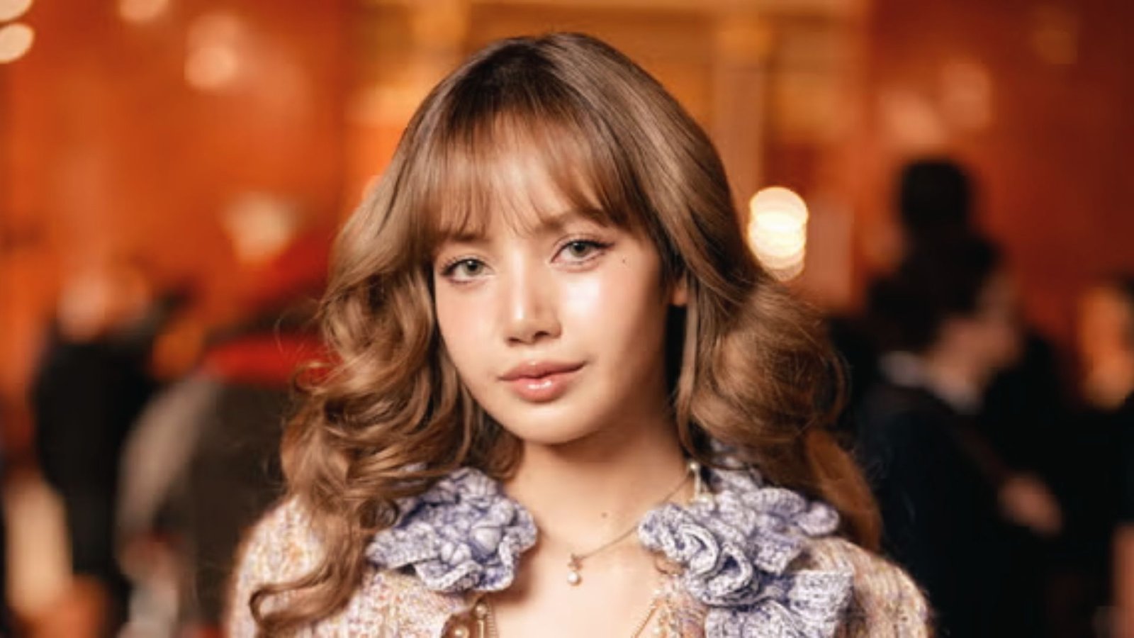 A young woman with butterfly cut hair and bangs, wearing a necklace, gazes thoughtfully at the camera.
