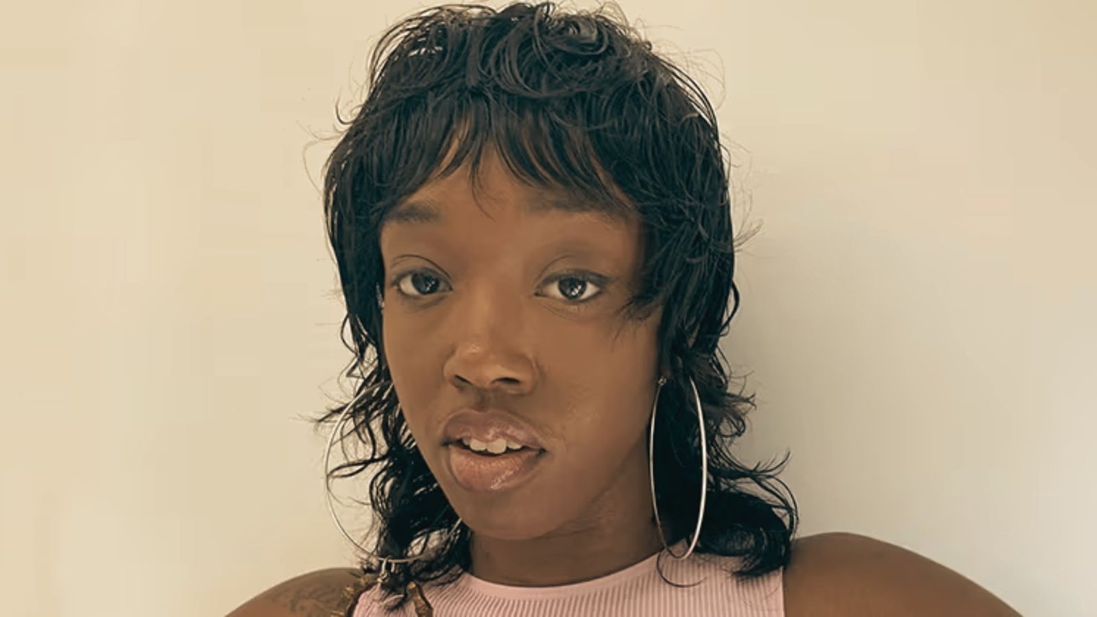 A woman wearing big earrings and a pink top, showcasing a wet look mullet hairstyle.