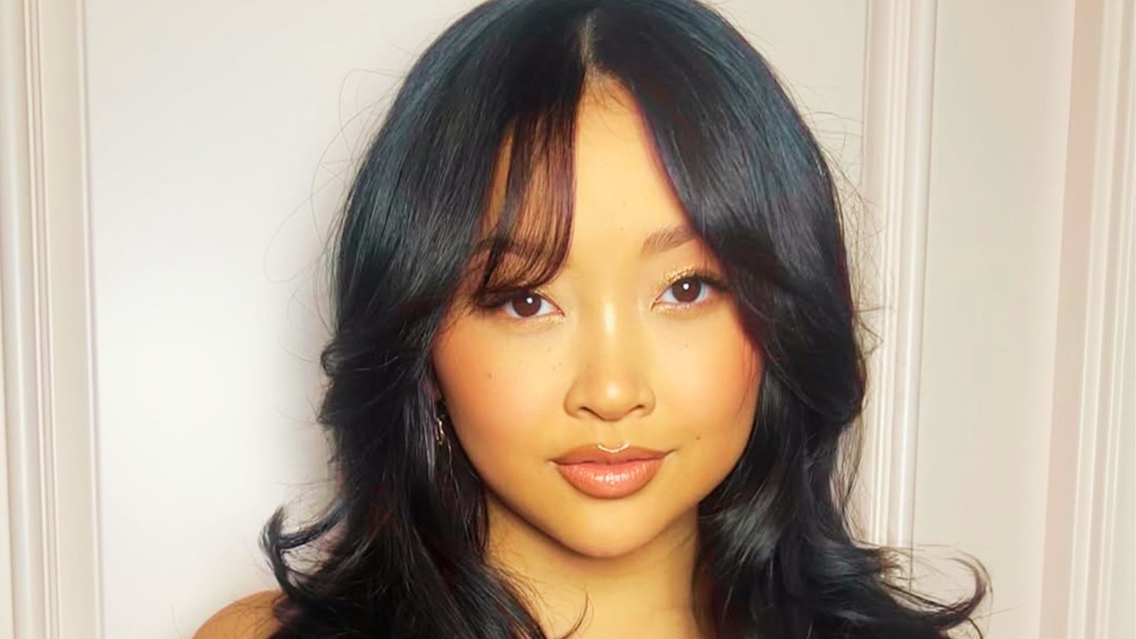 Woman with long hair and a fringe, styled in a half-updo with long layers and curtain bangs.

