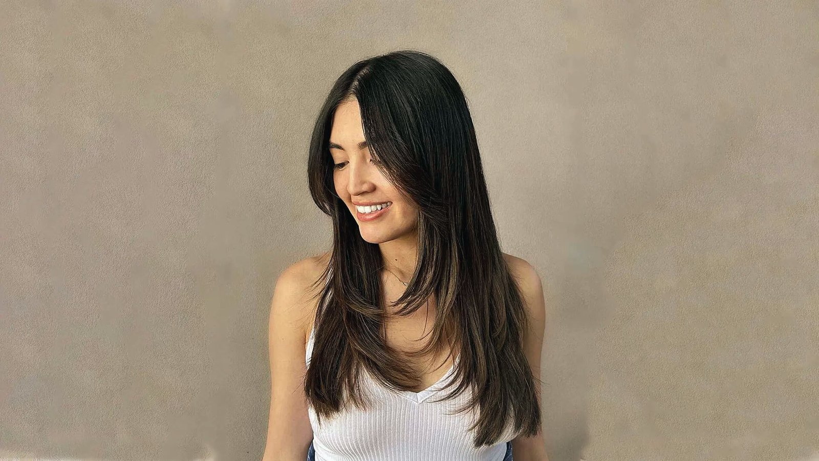 A woman with long, straight layered butterfly cut hair, smiling brightly and exuding joy.
