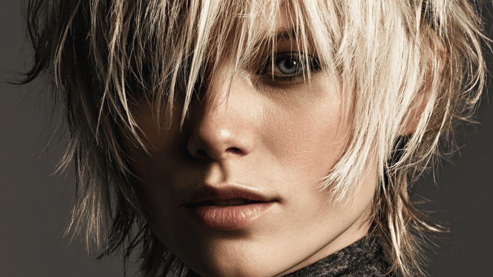 A woman with a choppy, layered pixie cut, featuring short blonde hair and bright blue eyes.