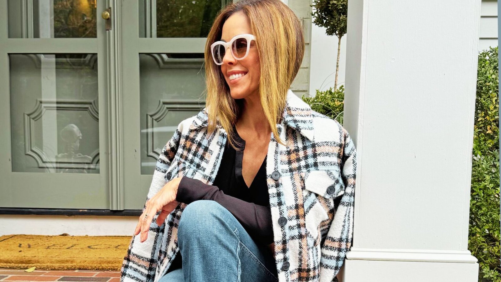 A woman in sunglasses and a plaid shirt sits on a step, looking relaxed and enjoying her surroundings.