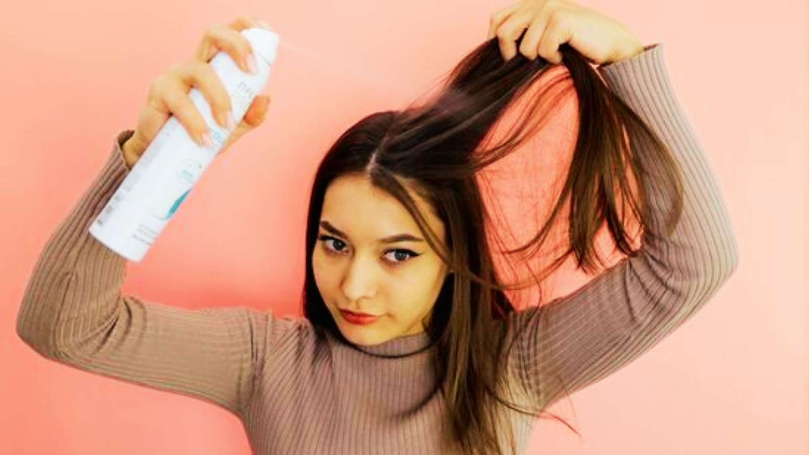 A woman holds a hair care product, preparing to style her hair with focused concentration.
