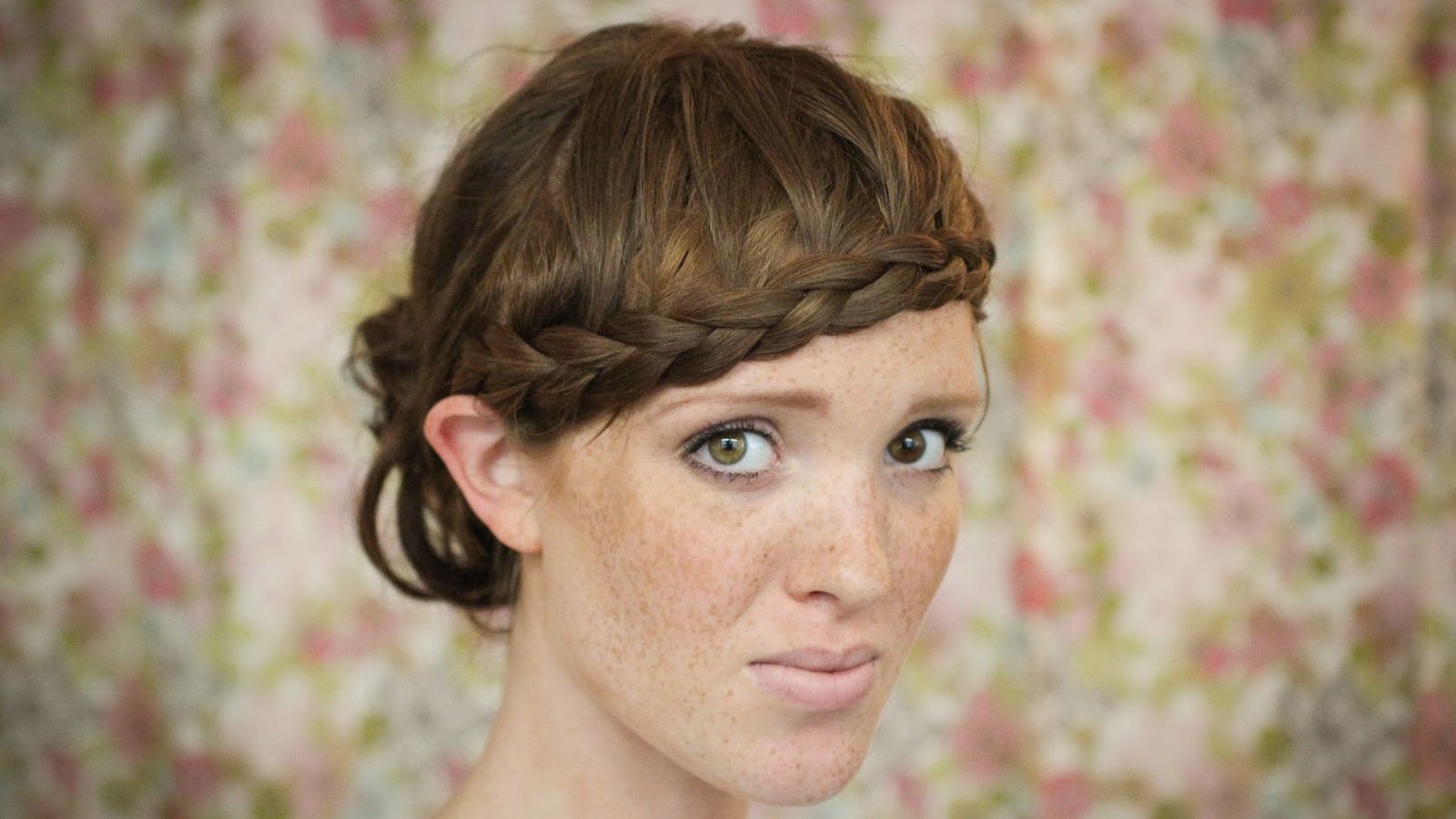 Woman with brown hair in a low bun and a braided headband across the forehead. The faux-bang braid replaces a traditional fringe for a romantic, bohemian style.