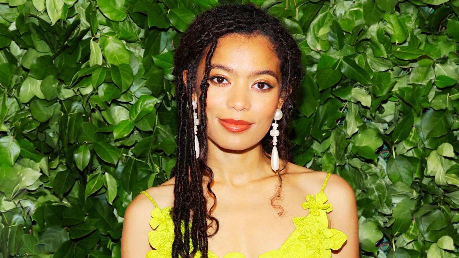 A woman with dreadlocks wearing a vibrant yellow dress, showcasing a stylish faux locs hairstyle.