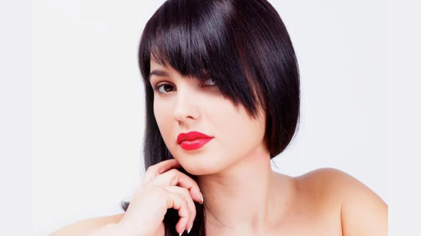 Woman with sleek black bob and asymmetrical side-swept bangs covering one eye. The fringe is longer on one side, tapering diagonally across the forehead for an edgy look.