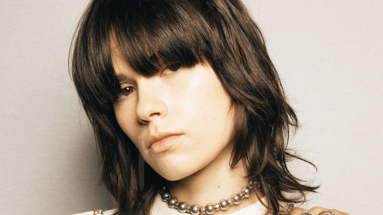 A woman with long hair styled in a modern shullet, wearing a stylish necklace.