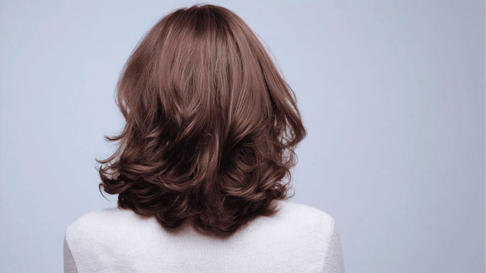 Back view of wavy shoulder length haircut with cascading layers in rich brown shade